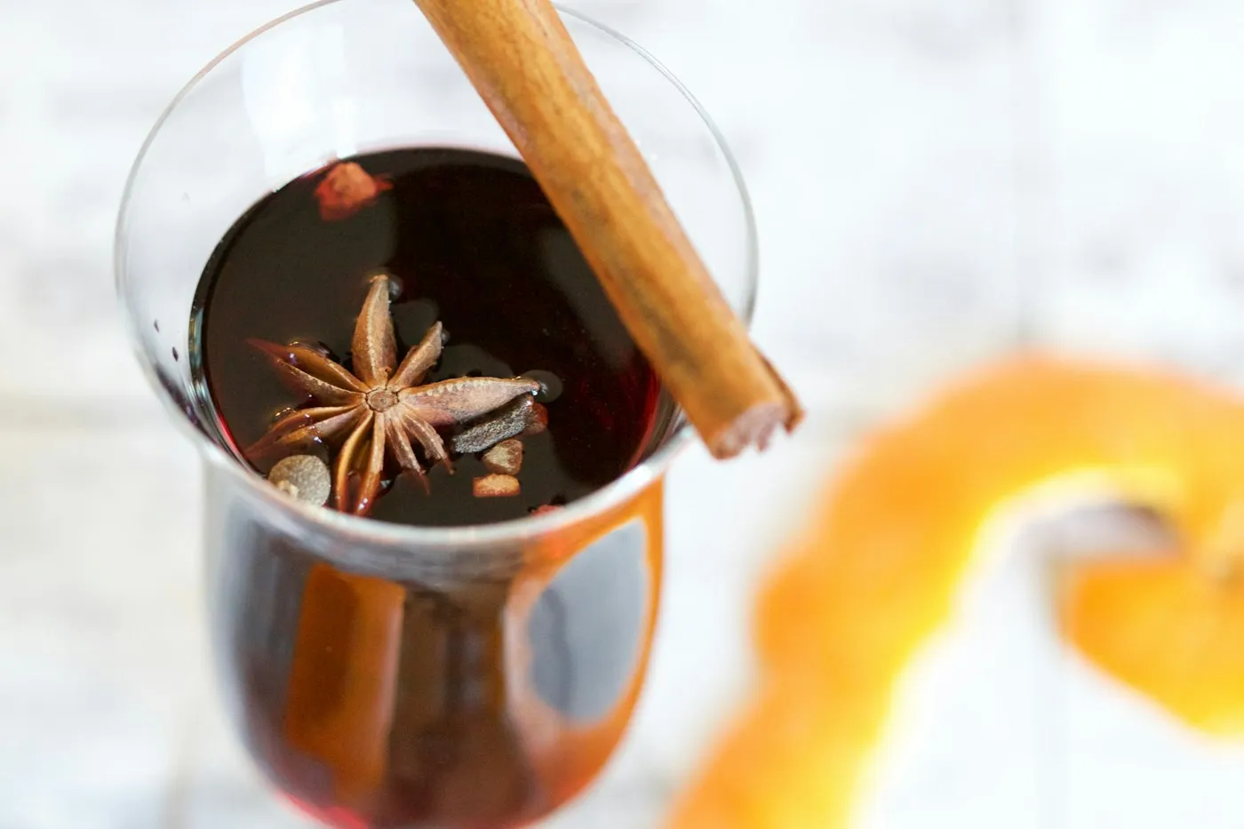 Et glas gløgg med stjerneanis og en kanelstang ved siden af en appelsinskal