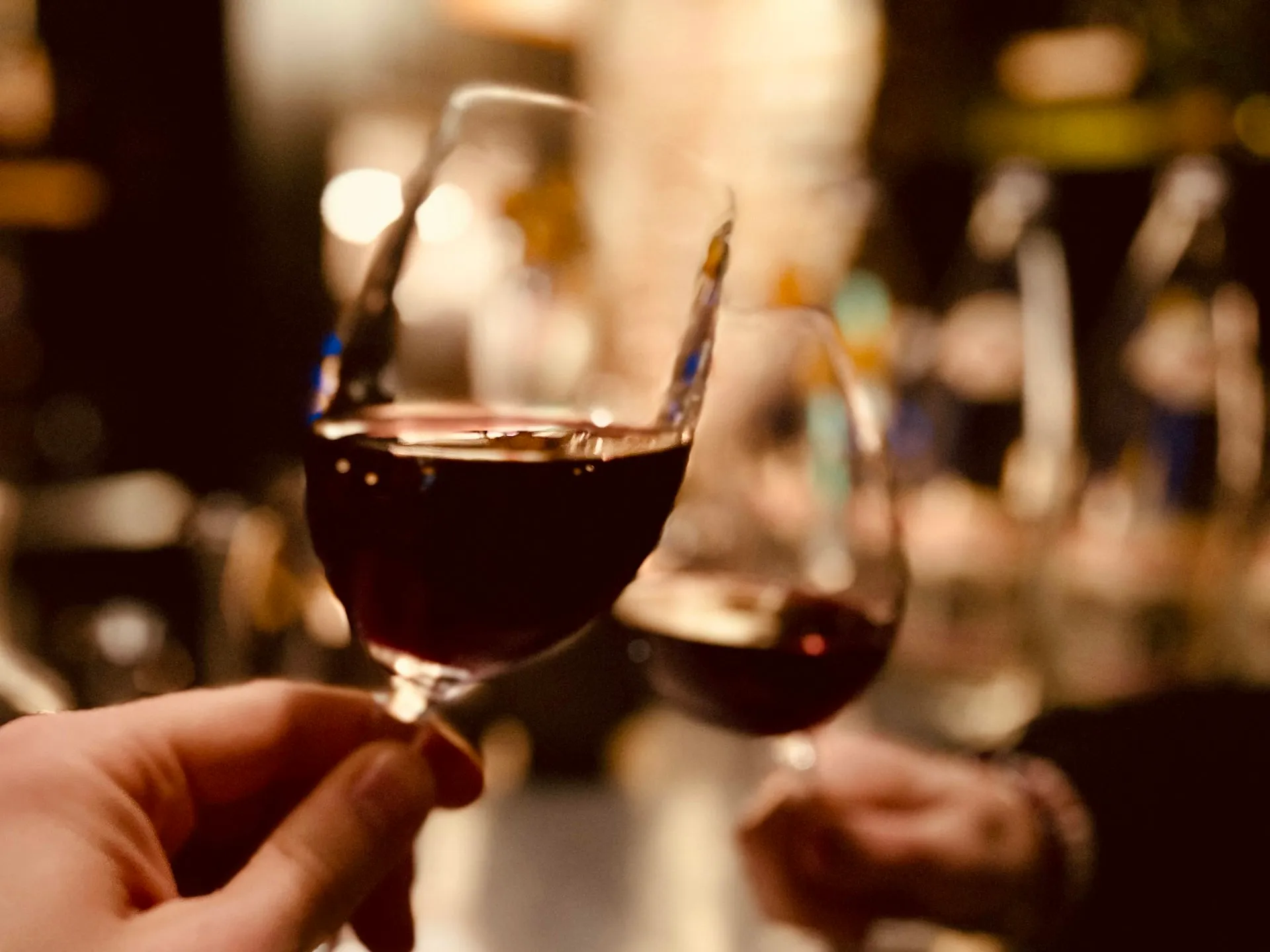 Et glas rødvin løftes i et varmt lys