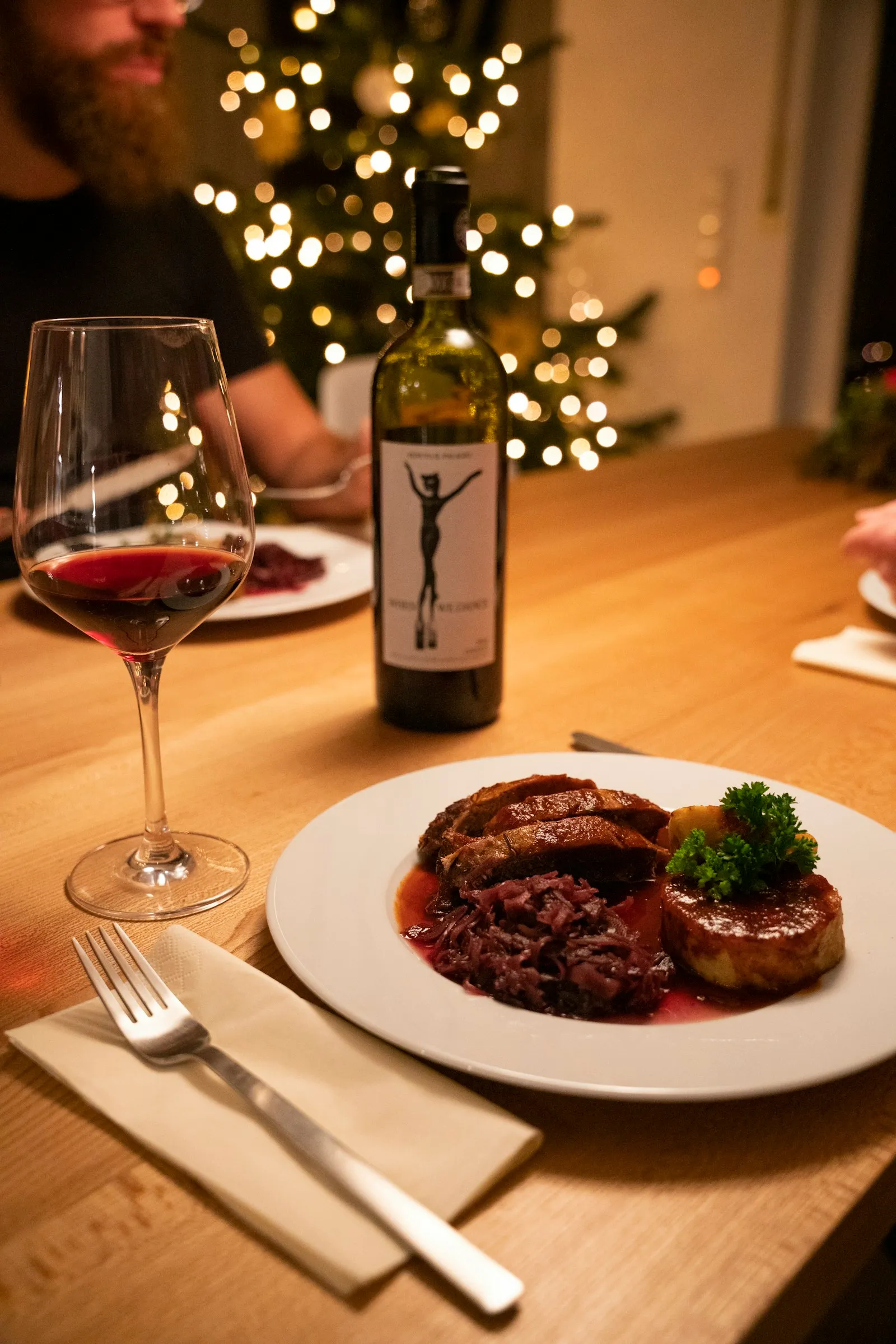 Julemiddag på en hvid tallerken ved siden af et glas rødvin og et juletræ